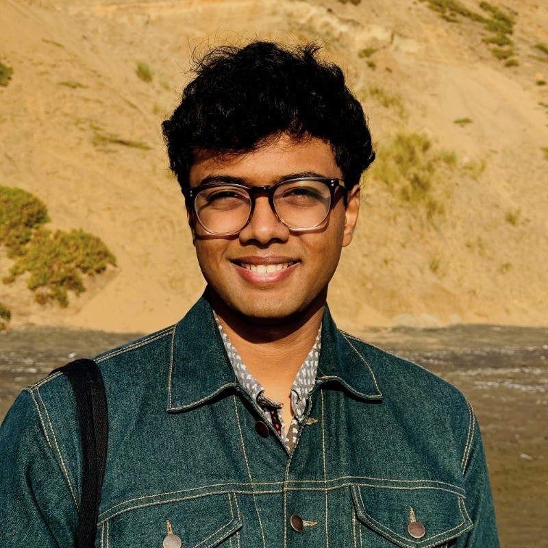 A photo of Tarun smiling with a sandy natural background.