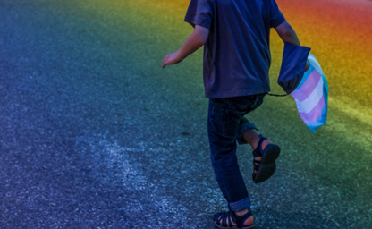 An image of a person running on a rainbow road and holding a transgender flag.